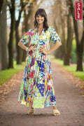 Woman in floral Orientique Kiana Peak Dress walking on a tree-lined path, showcasing summer style and elegance.