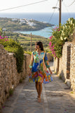 Model wearing Sardinia Layers Frill Sleeve Dress walking down a picturesque street with vibrant surroundings.