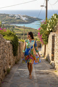 Model wearing Sardinia Layers Frill Sleeve Dress walking down a picturesque street with vibrant surroundings.