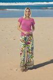 Model wearing Orientique Ovahe Pant in vibrant tropical print on a beach.