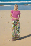 Model wearing Orientique Ovahe Pant in vibrant tropical print on a beach.