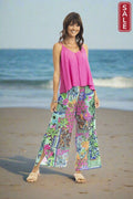 Model in a beach setting wearing Maeli Pink Pant and a pink top, showcasing vibrant summer style.