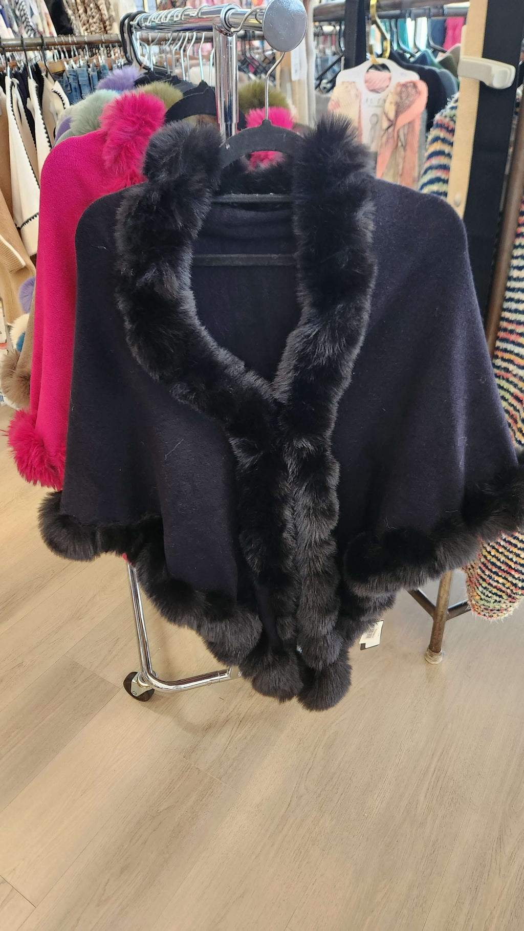 Camilla Shawl showcasing a luxurious cape design with plush faux fur trim in a stylish boutique setting.
