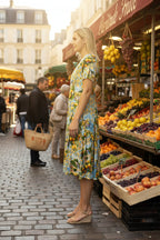 Amalfi Dress Godet Short Sleeve displayed in a vibrant market setting, showcasing its flowing design and summer style.
