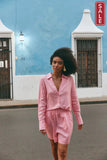 Sojourn Linen shorts in a stylish pink ensemble walking by a colorful building with a SALE sign.