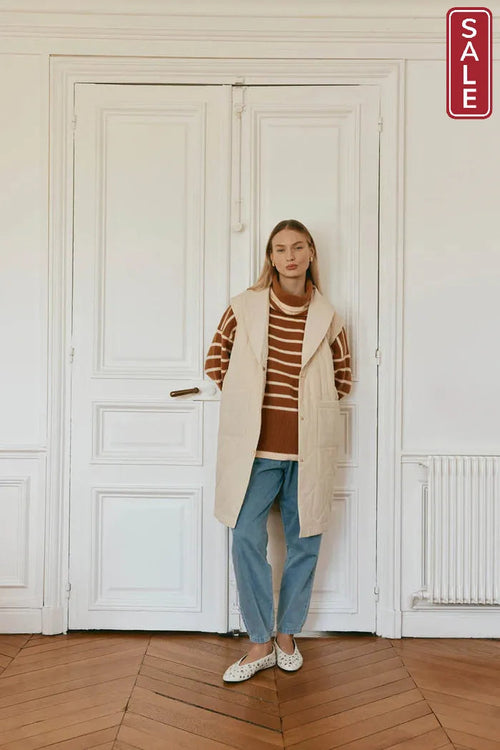 A model showcasing the Argo Longline Vest Ecru over a striped sweater, highlighting its stylish layered look.
