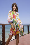 Woman in Erica Tiered Dress with tropical prints, posing by the beach on a sunny day.