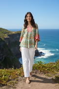 Woman wearing Araya Top V Flaired Sleeve, standing near the ocean with flared sleeves and vibrant patterns.