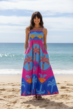 Celeste Blue Strappy Dress worn on a beach, showcasing its vibrant colors and palm tree print.