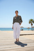 Model wearing WT Button Pant on a sunny beach boardwalk, showcasing stylish white tailoring.