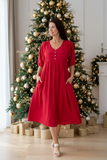 Model wearing WT Red Peasant Dress, a red midi dress with V-neck and front button details, beside a Christmas tree.