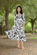 A woman wearing the Cora Dress black/white by Willow Tree, set against a lush, green background.