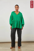 Woman modeling the Panorama Relax Top-meadow in vibrant green, paired with stylish black pants, perfect for winter styling.