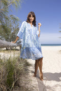 Woman wearing the Carla Layers Dress while standing on the beach, showcasing its blue mosaic print and relaxed style.