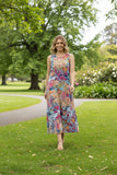 Model wearing Ikebana Sleeveless dress in a colorful floral print, walking through a lush green park.