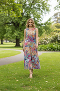 Model wearing Ikebana Sleeveless dress in a colorful floral print, walking through a lush green park.