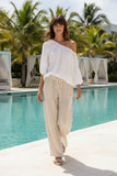 Model wearing Linen Solid Pant Wide Leg by Orientique, strolling by a pool in a sunny tropical setting.