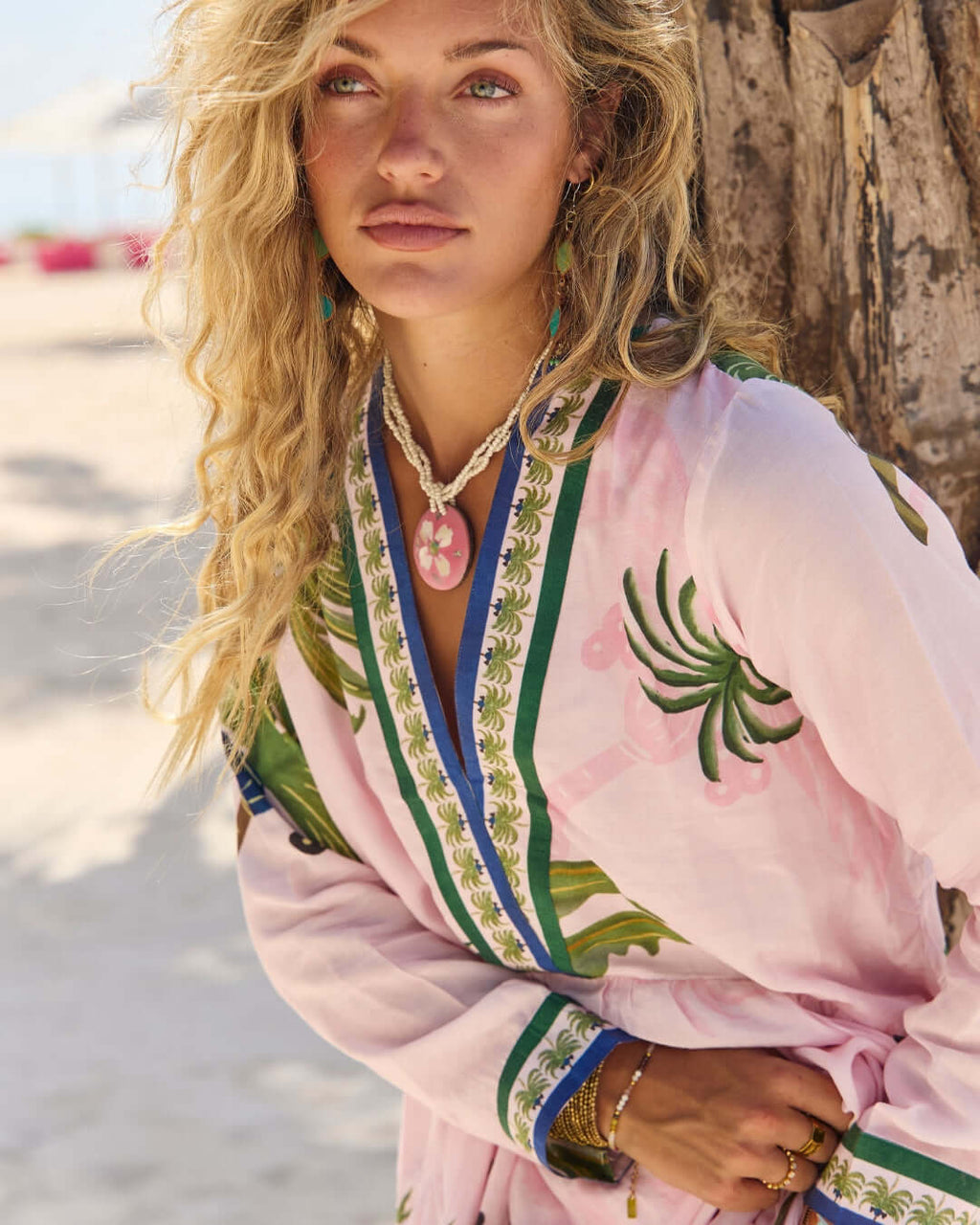 Model wearing the Penelope Maxi Amazon by Naudic with pink and green Amazon print on a beach.