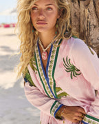 Model wearing the Penelope Maxi Amazon by Naudic with pink and green Amazon print on a beach.