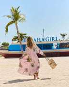 Woman wearing Penelope Maxi Amazon dress walking on the beach with palm trees in the background.