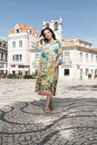 Model wearing the Amalfi Collar Dress in a vibrant floral print, standing on a cobblestone street under a clear blue sky.