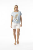A model wearing the Le Soleil chambray Top in soft blue with a stylish front design, paired with white shorts.