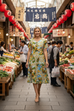 Woman wearing Amalfi Dress Godet Short Sleeve in vibrant print, walking through a lively market with fresh produce.