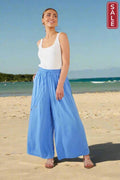 Woman wearing Florence Pants Coast in blue on the beach, showcasing laid-back summer style.