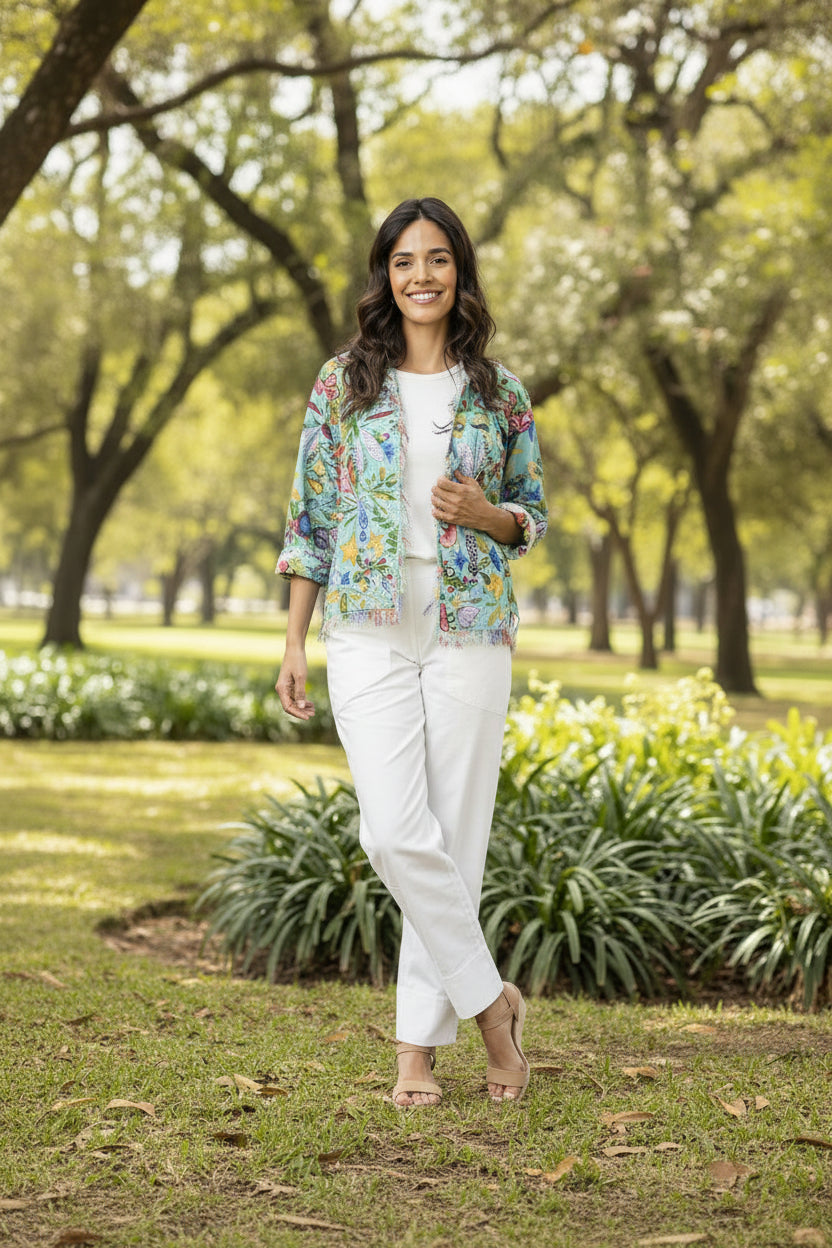 Woman in Sante Fe Jacket 2 walking in a park surrounded by greenery on a sunny day.