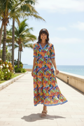 Woman in vibrant tropic print Bianca Maxi Dress strolling by the beach with palm trees.