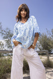 Model wearing Carla Tassel Top Blue with relaxed white pants on a sunny beach.