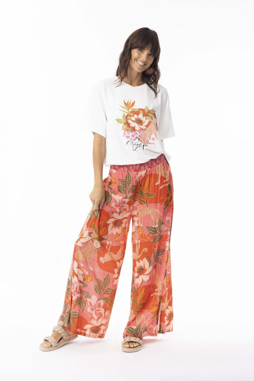 Model wearing Aria Pants with vibrant floral print and a white floral tee, showcasing summer style and comfort.