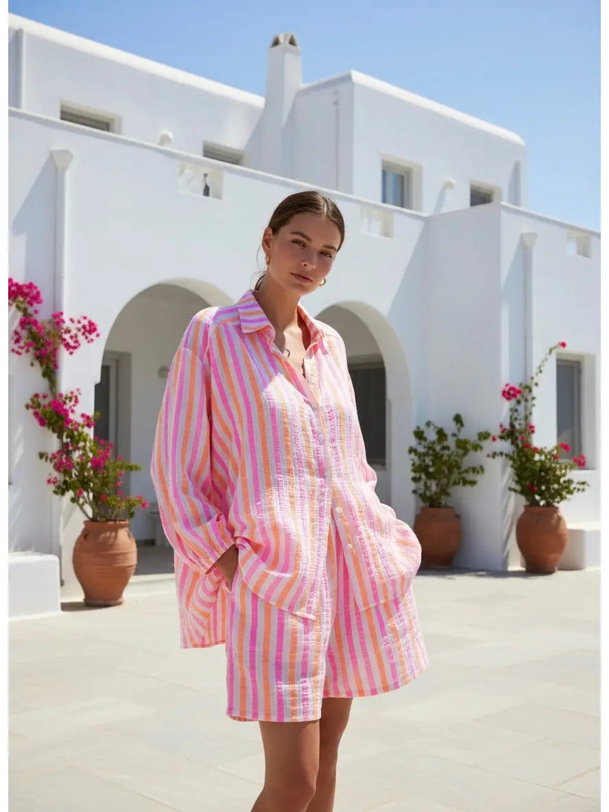 Model wearing candy striped shorts in pink, white, and orange, standing outdoors in a sunny setting.
