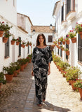 Woman walking in a picturesque alley wearing AT Leaf Pant, a stylish blend of linen and rayon with a breezy fit.