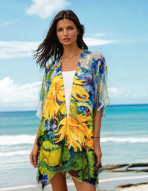 Model wearing Atn Cape Verde cape with vibrant floral print by the beach, showcasing summer elegance.