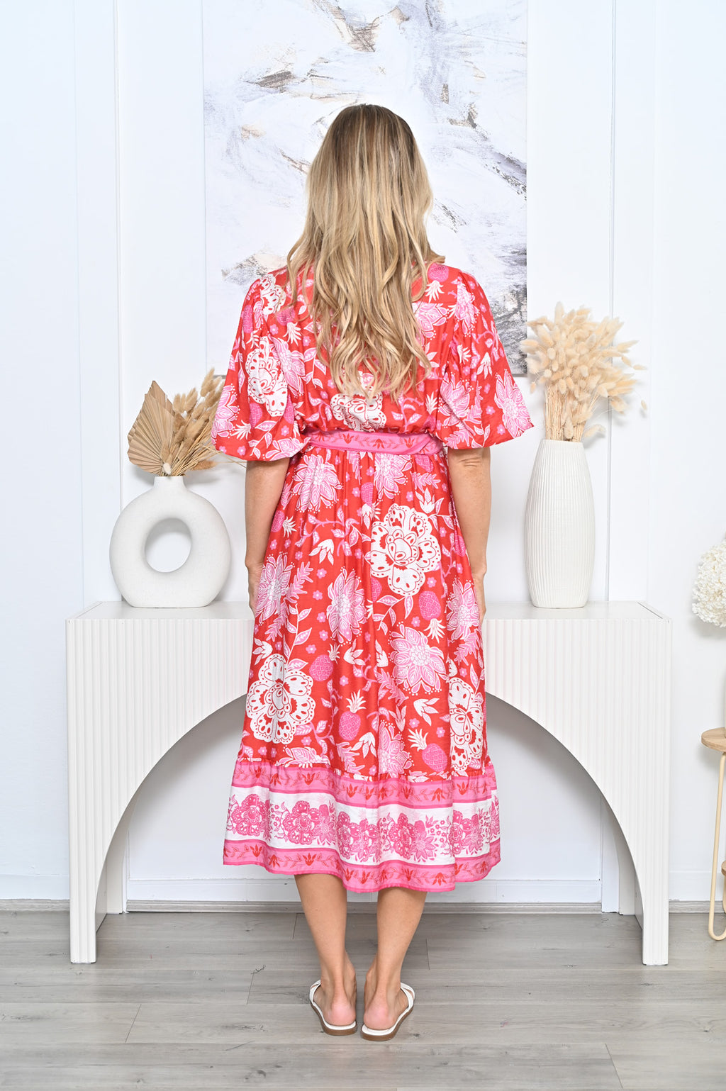Back view of a model wearing the Pineapple Shirt Dress red with floral patterns and a belted waist.