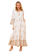 Model wearing Ketia Tiered Dress featuring cream fabric with gold details and flared sleeves.