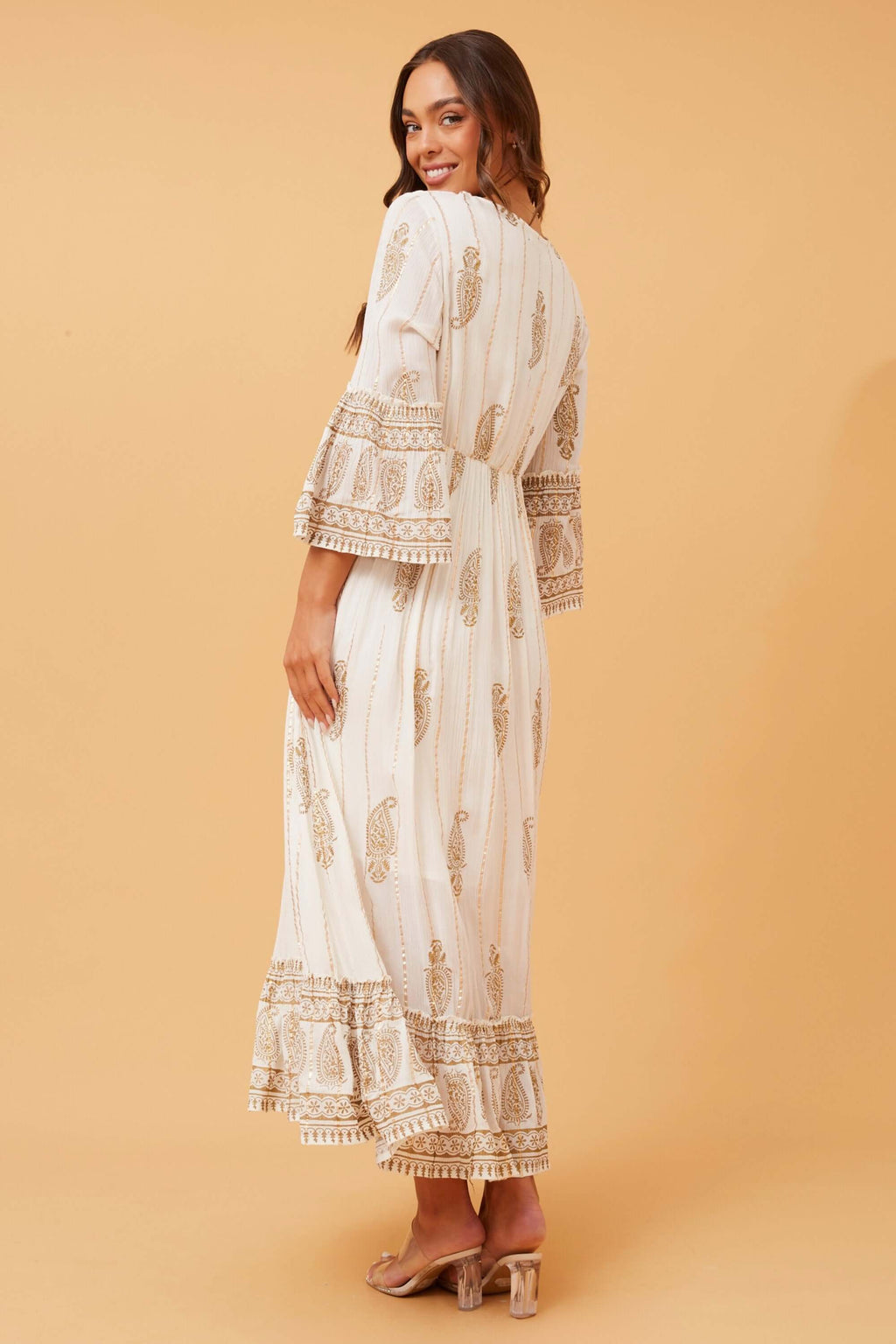 Back view of the Ketia Tiered Dress with cream fabric, gold details and flared sleeves. Perfect for any occasion!