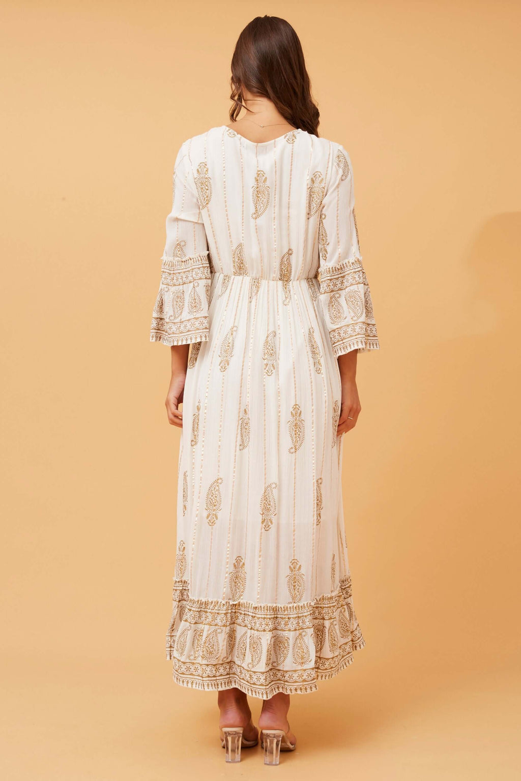 Back view of the Ketia Tiered Dress featuring cream fabric with gold details and 3/4 flared sleeves.