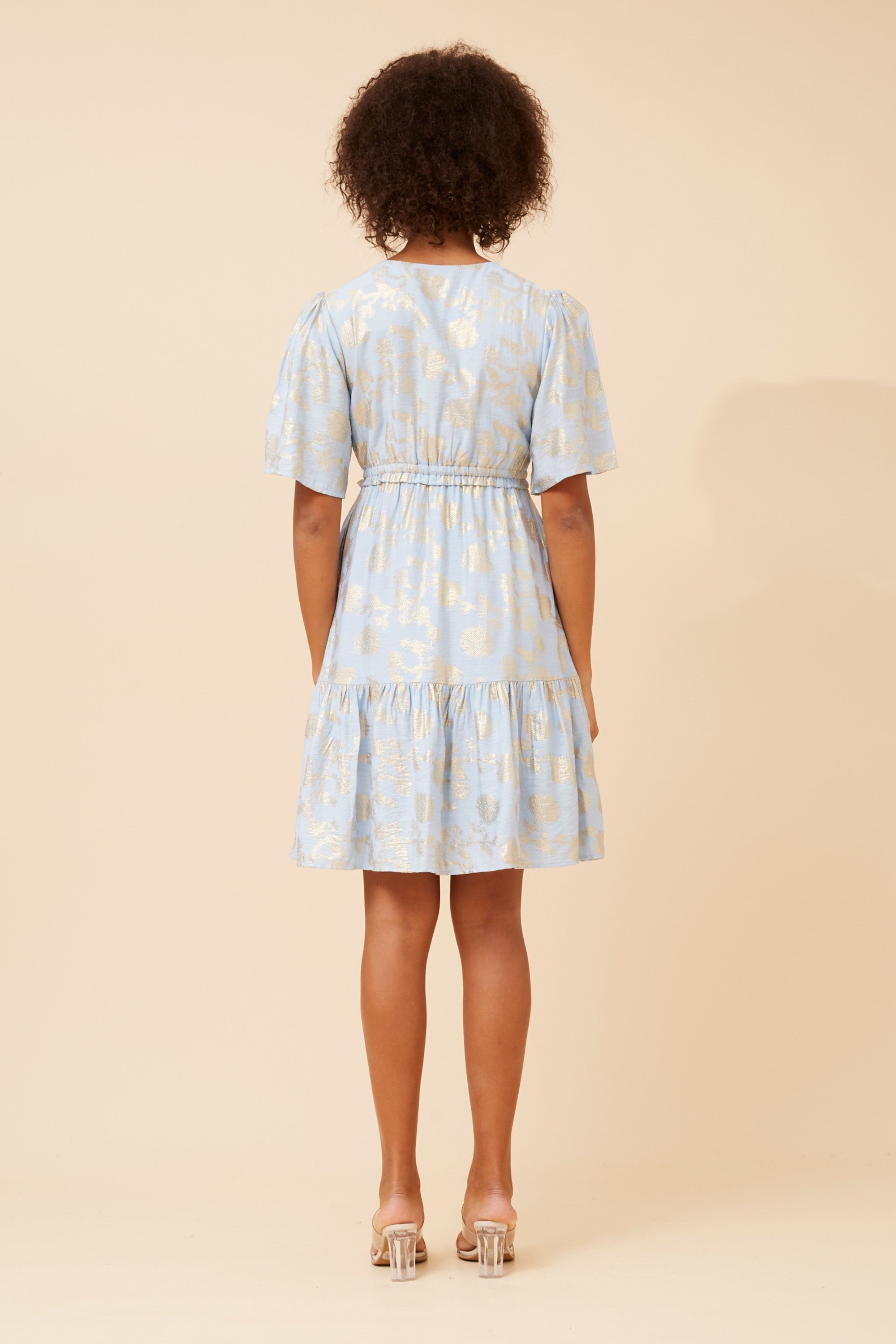 Back view of a model wearing the Gold Foil Dress, featuring a soft pale blue base with gold foil print.