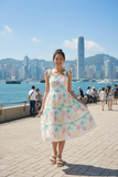 Model wearing a Coral Tie Strap Dress with floral patterns, set against a vibrant city skyline.