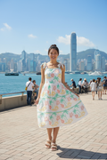 Model wearing a Coral Tie Strap Dress with floral patterns, set against a vibrant city skyline.