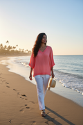Woman in a coral Barika V neck top walking on the beach at sunset, embodying elegant summer style.
