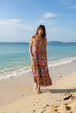 Francesca Strappy Dress in a vibrant kaleidoscope pattern worn by a woman on a sunny beach.