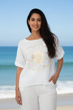 Model wearing the Golden Flower Linen Top with gold flower detail by the beach, showcasing elegance and comfort.