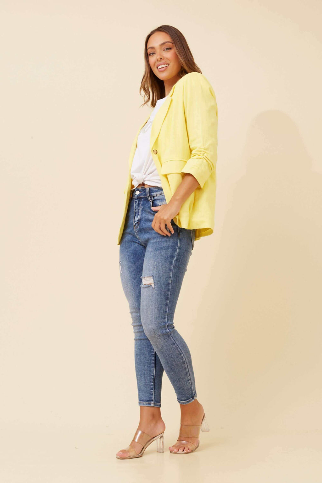 Woman wearing a Limoncello Linen Blazer in lemon yellow with blue jeans, styled for a chic look.