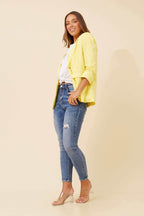Woman wearing a Limoncello Linen Blazer in lemon yellow with blue jeans, styled for a chic look.