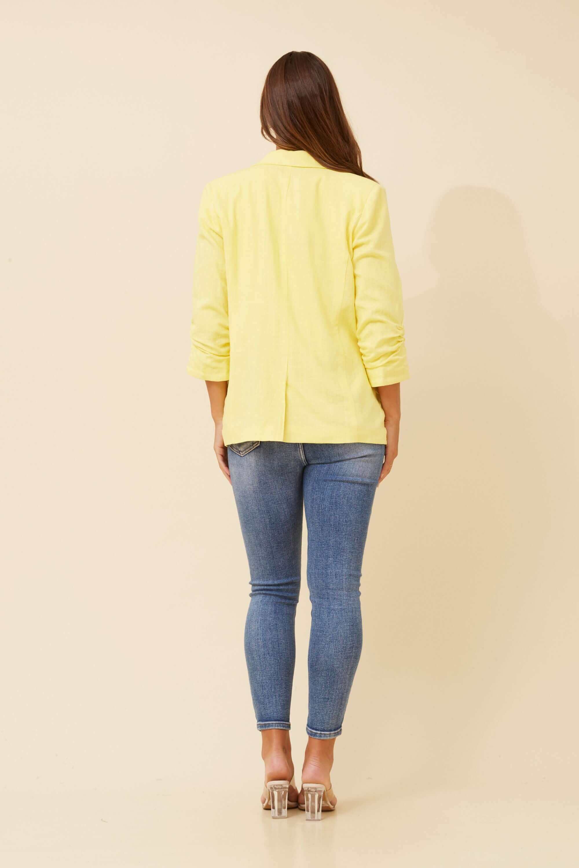 Back view of Limoncello Linen Blazer in lemon yellow, paired with skinny jeans for a chic look.