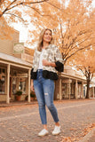 Woman wearing a stylish Jaipur Shirt with jeans, standing on a charming street lined with autumn trees.
