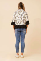 Back view of a woman wearing a floral Jaipur Shirt with blue jeans and white shoes on a beige background.